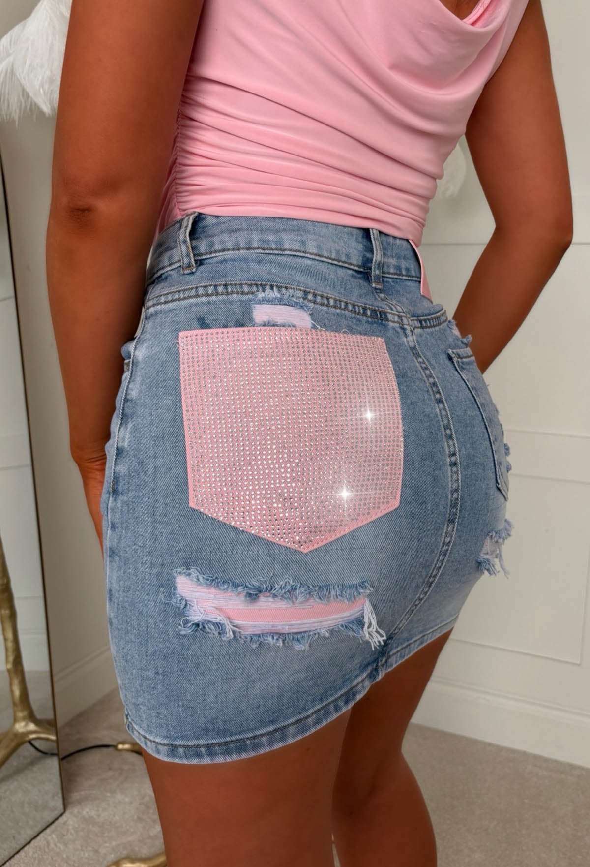 Mid wash stretch denim mini skirt with pink crystal embellished back pocket and distressed details.