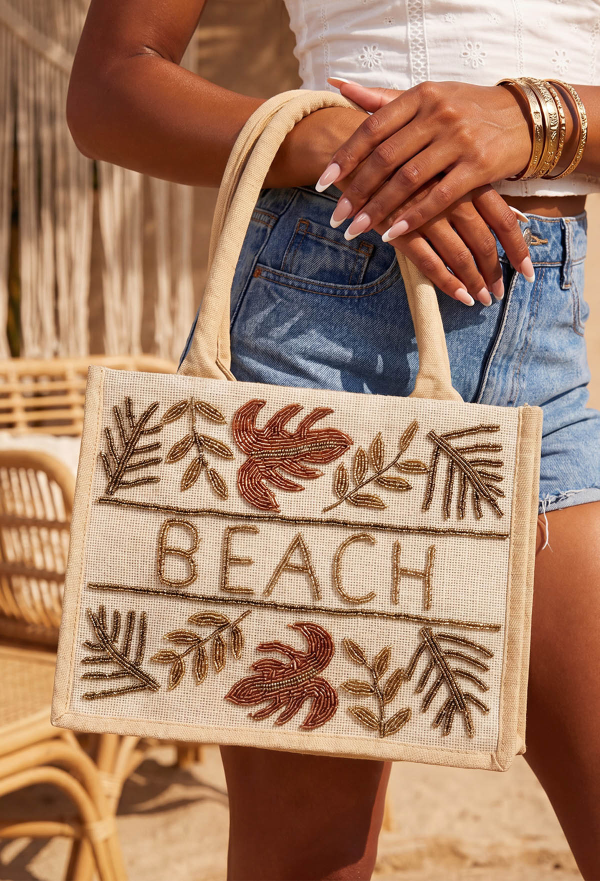 Beige beach beaded bag with sturdy handles, beaded leaf details and BEACH lettering on the front.