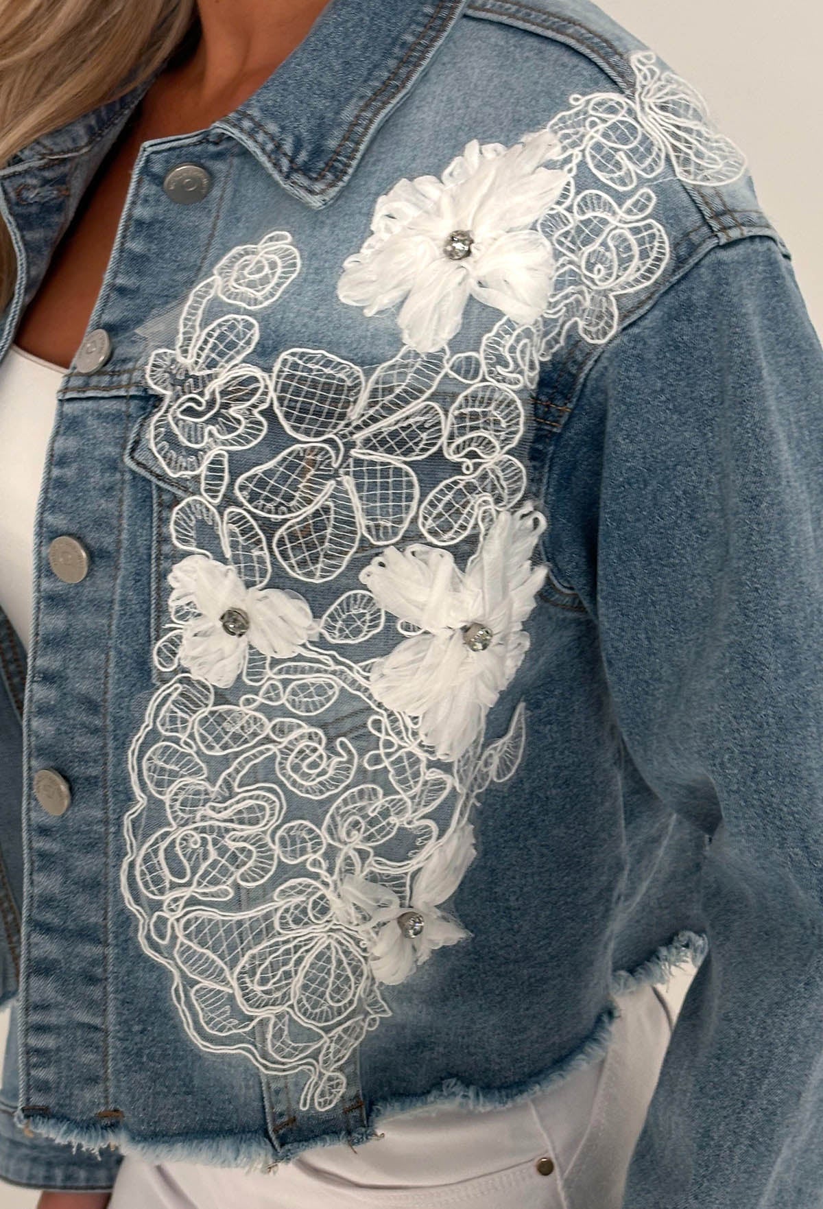Mid wash stretch denim jacket with white lace panels, floral appliqué and a cropped raw hem.
