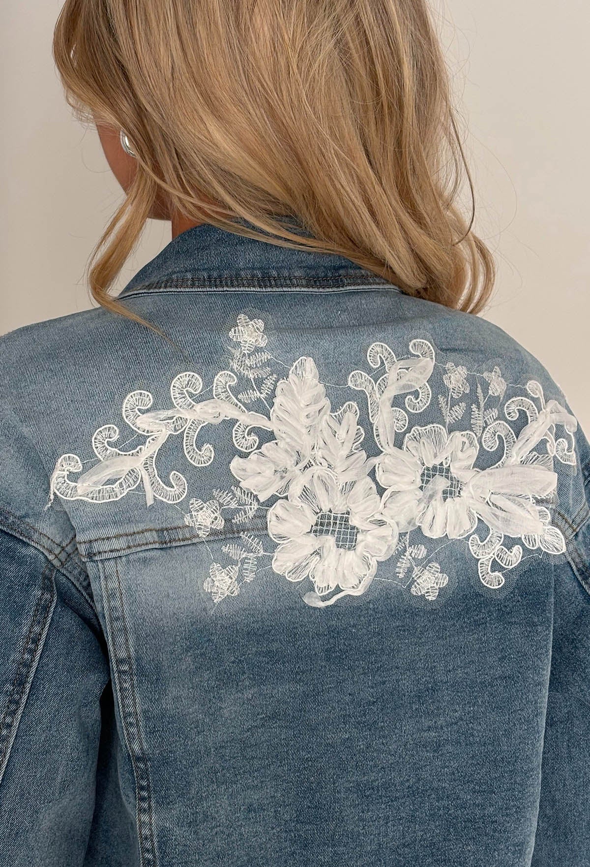 Mid wash stretch denim jacket with white lace panels, floral appliqué and a cropped raw hem.