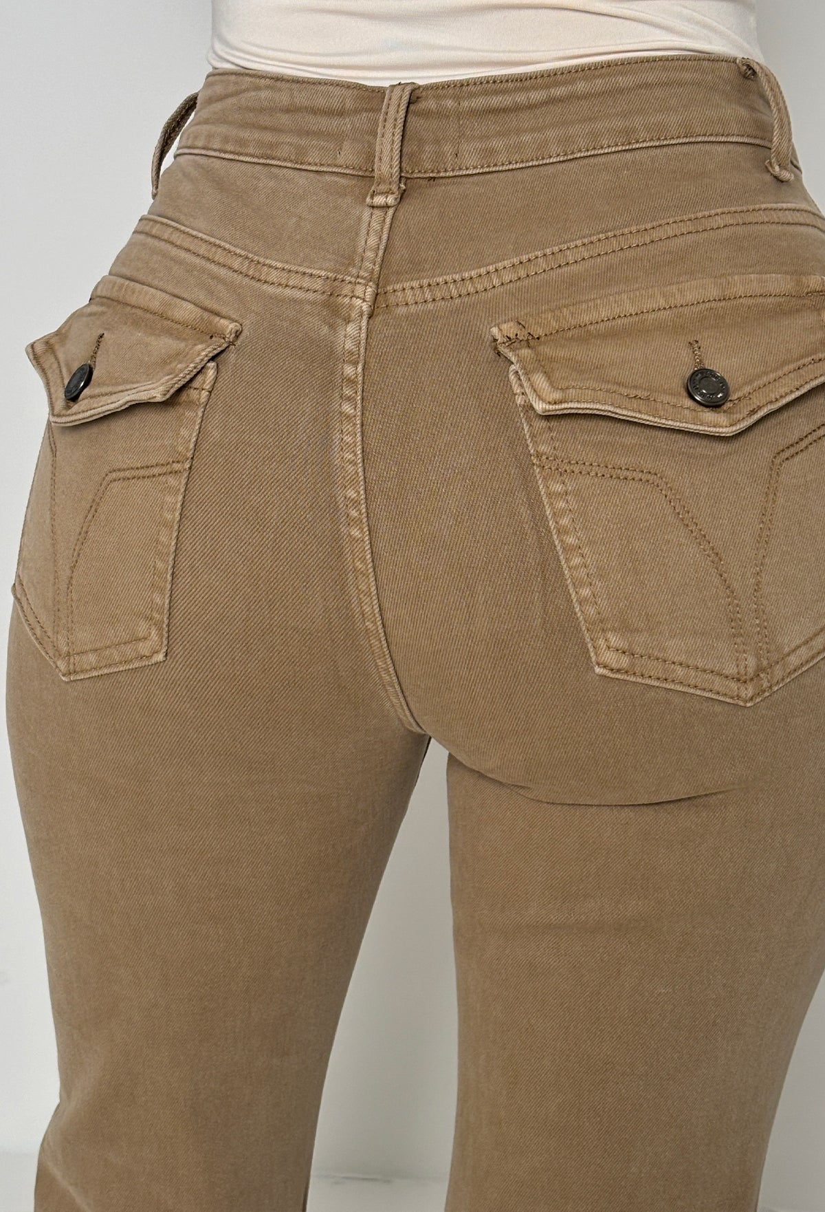 Back view of beige stretch fitted and flared mid rise jeans with flap back pockets and subtle seam detailing.