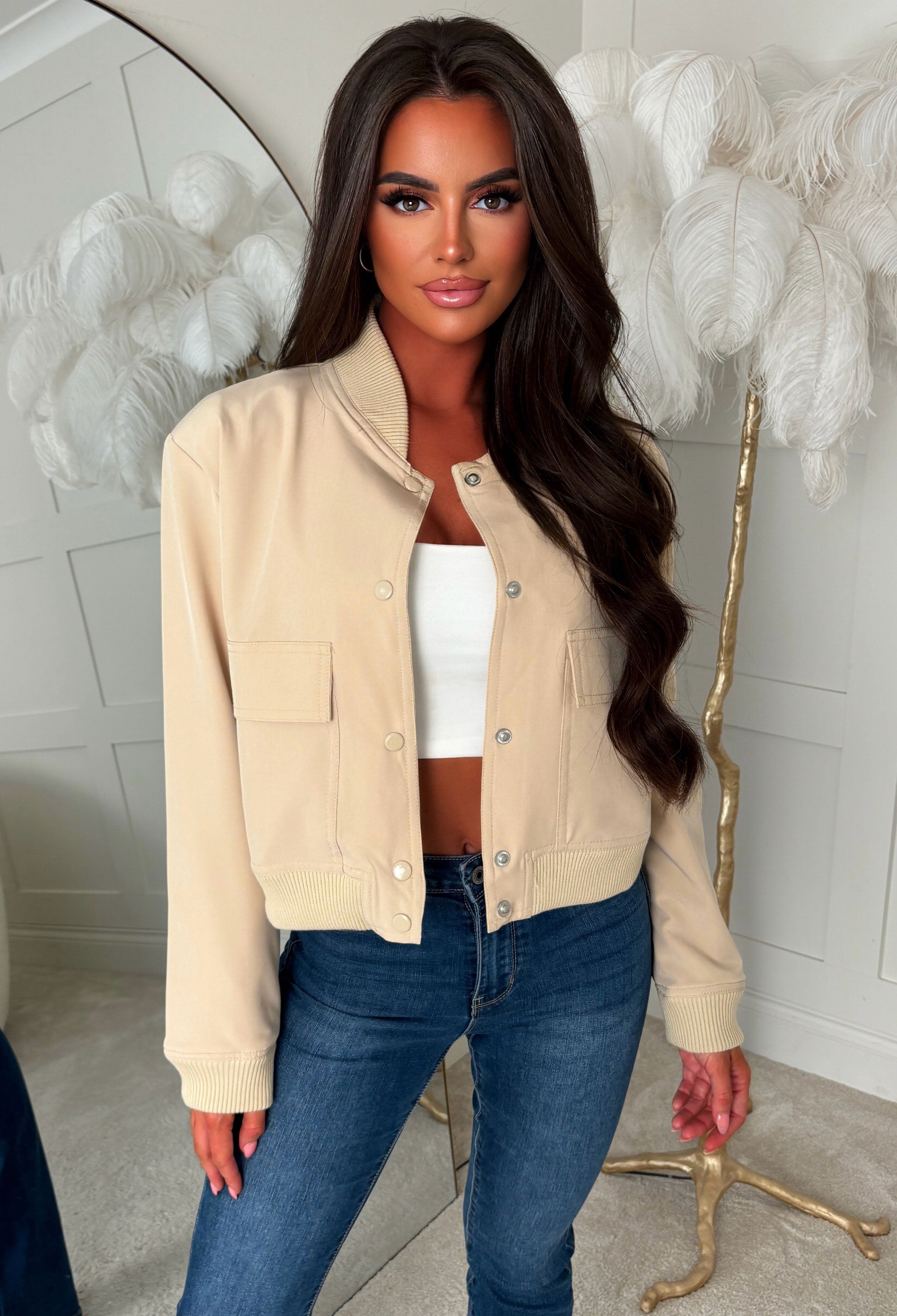 Beige front pocket bomber jacket with silver popper fastening, ribbed cuffs and hem, styled with light blue jeans.