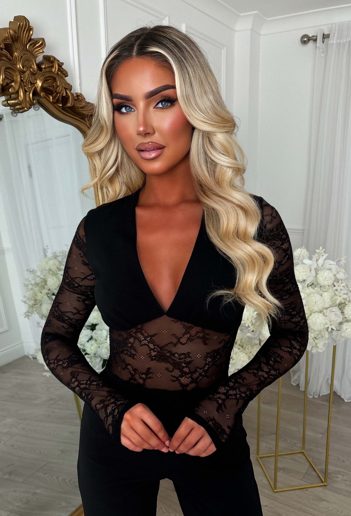 Black lace longsleeve jumpsuit with sheer floral lace sleeves, plunging neckline and fitted legs.
