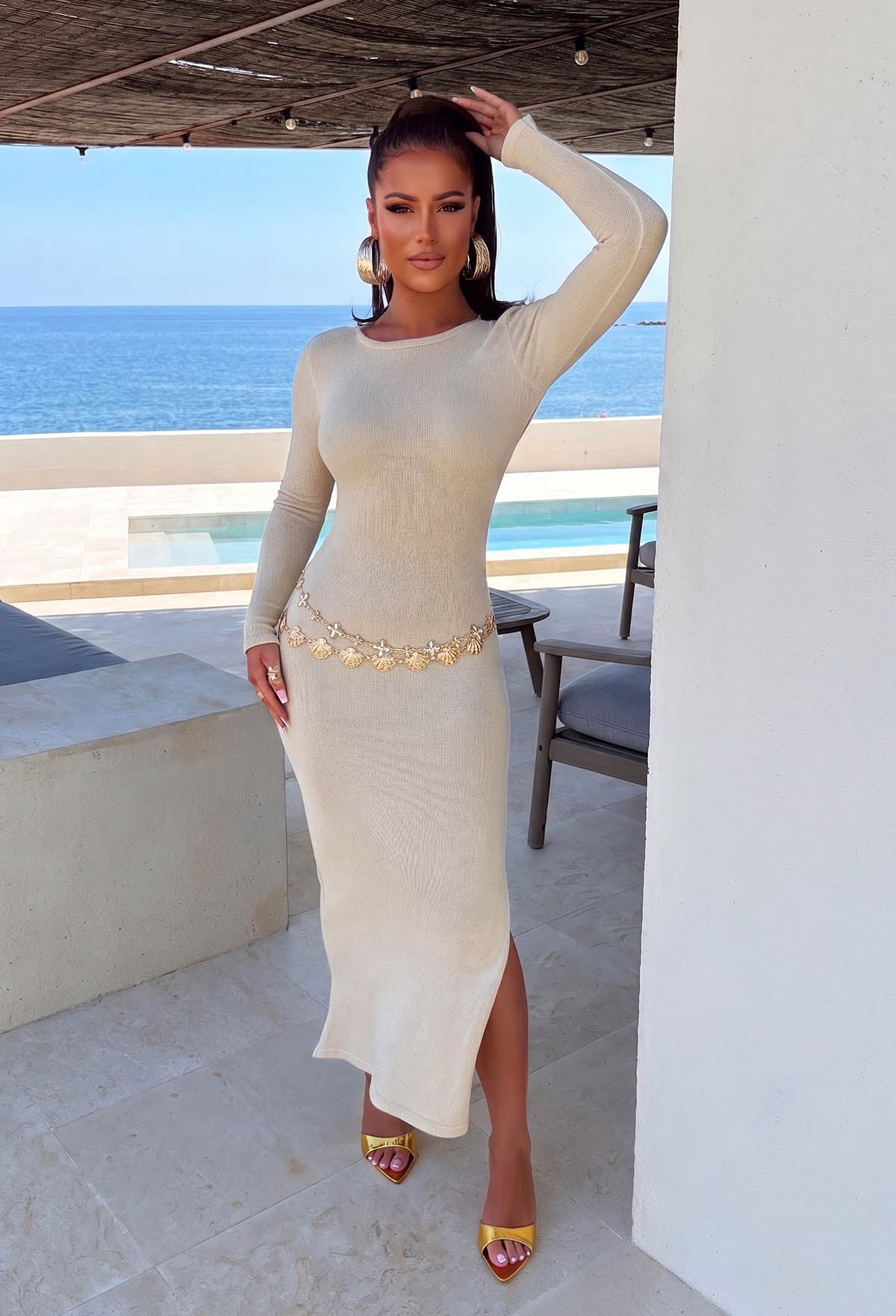 Back view of a gold lurex backless knitted dress with long sleeves, shimmering finish and side split hem.