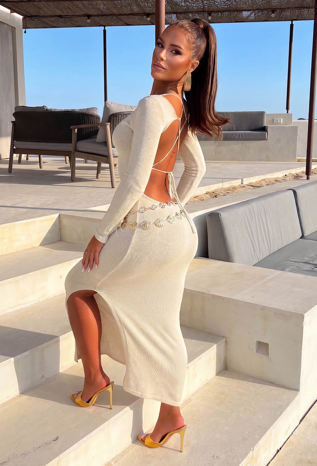Back view of a gold lurex backless knitted dress with long sleeves, shimmering finish and side split hem.