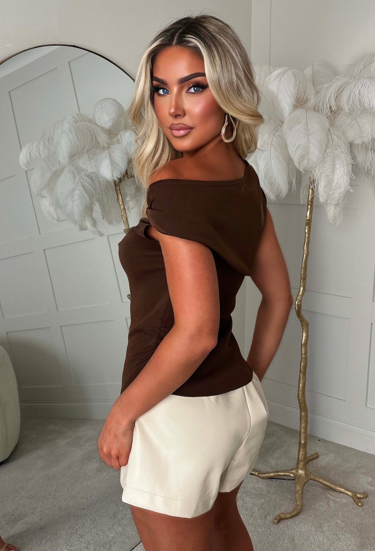 Brown off the shoulder knit top with gold tone detail at the shoulder and a fitted silhouette.
