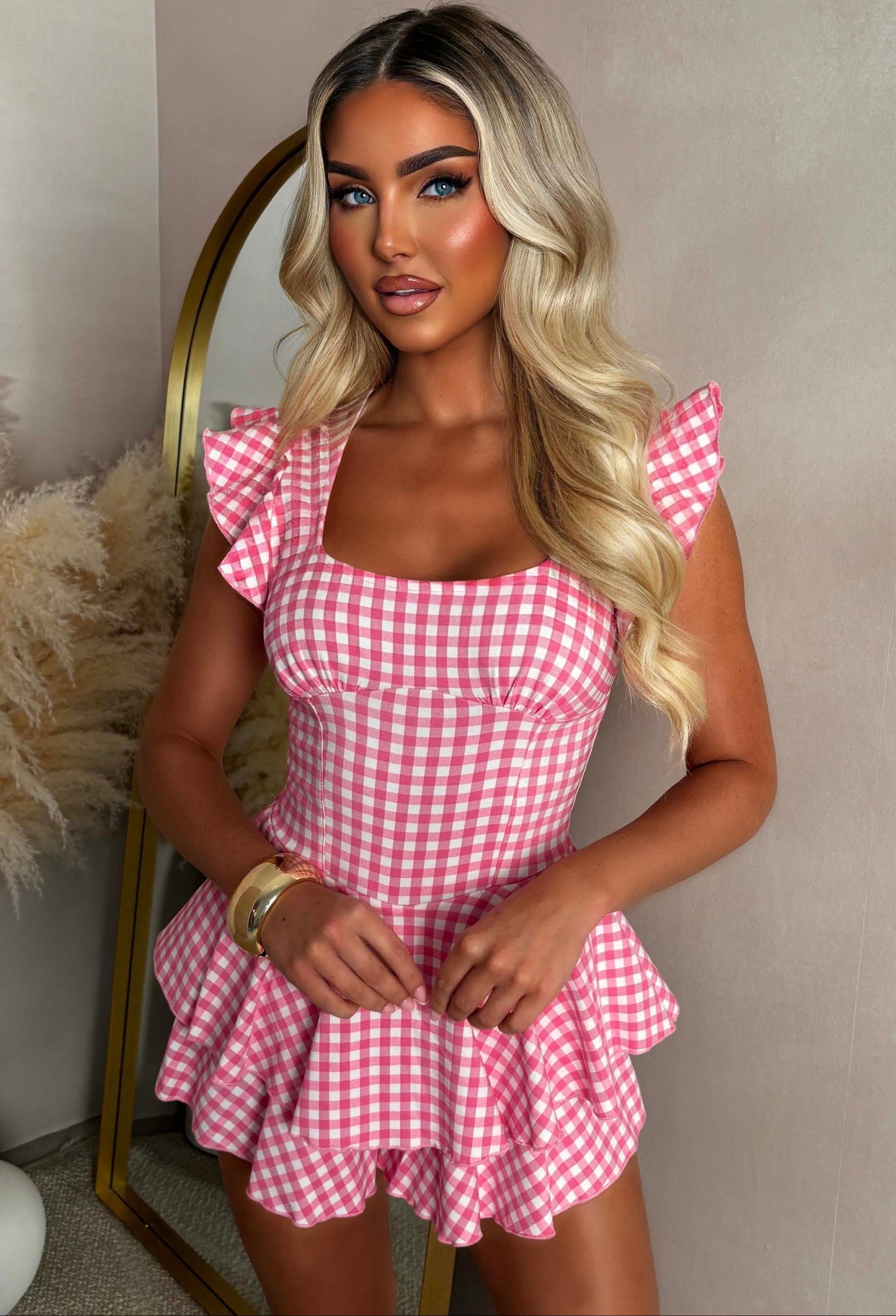 Model wearing a pink gingham playsuit with a square neckline, ruffle detailing and a relaxed fit, perfect for a feminine summer look. close up shot
