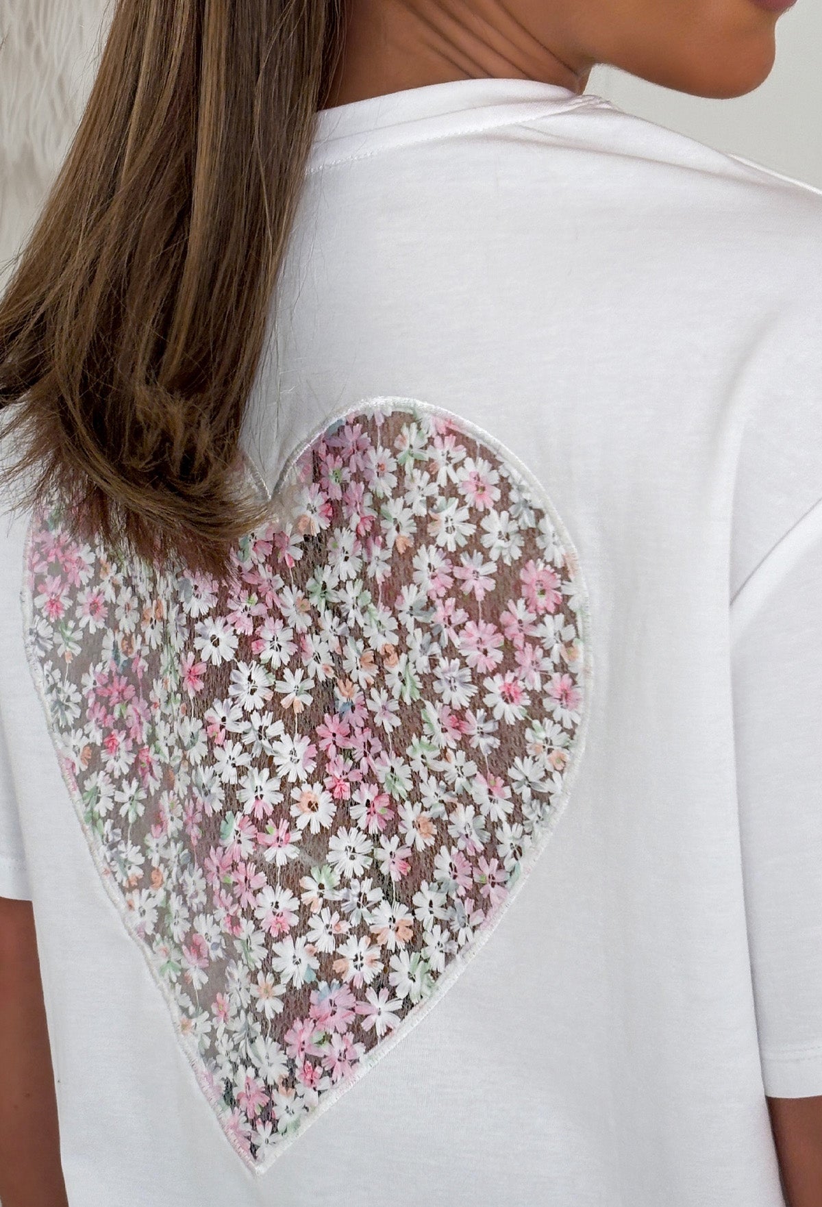 Back view of a white oversized T-shirt with an embroidered floral heart design.