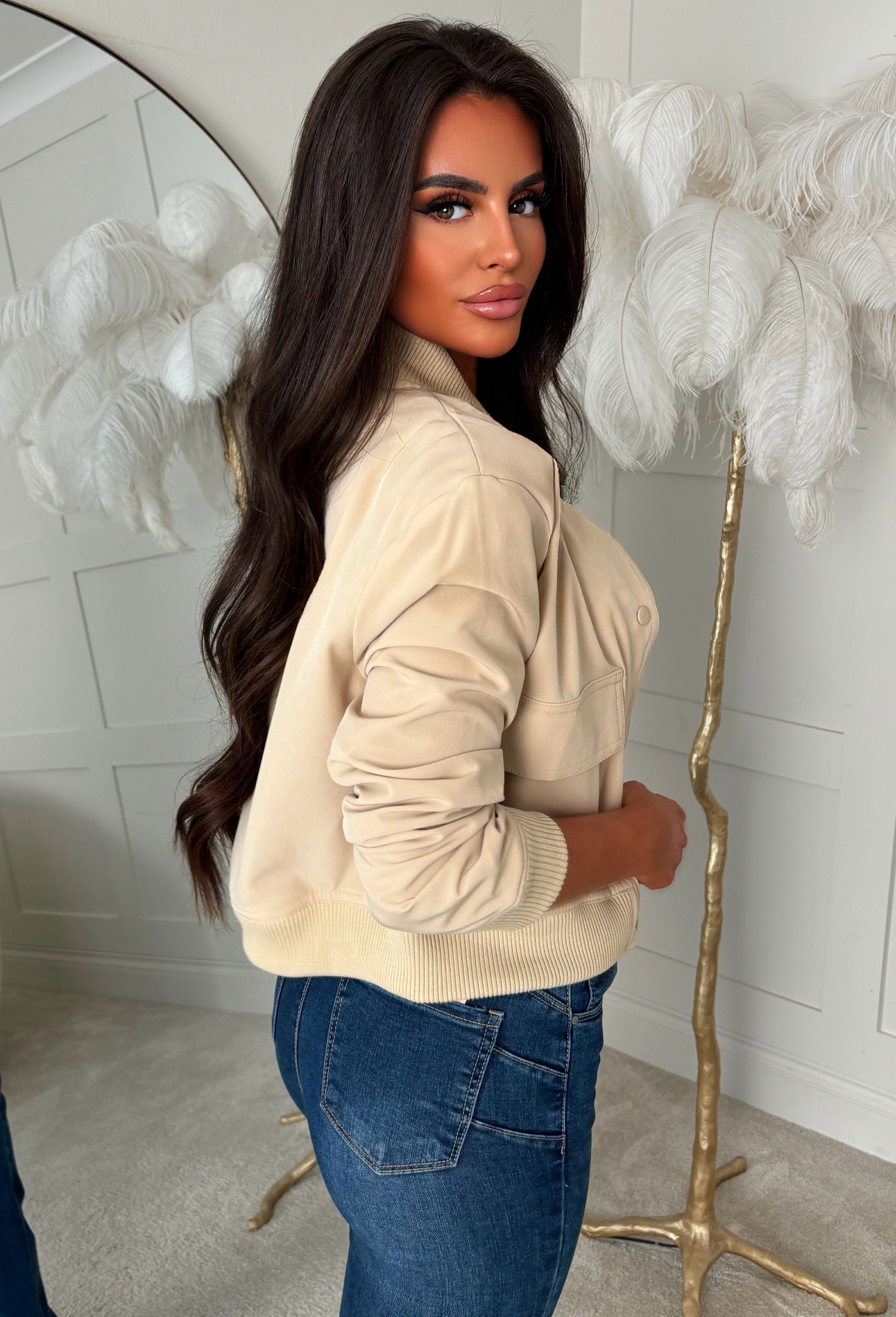 Beige front pocket bomber jacket with silver popper fastening, ribbed cuffs and hem, styled with light blue jeans.