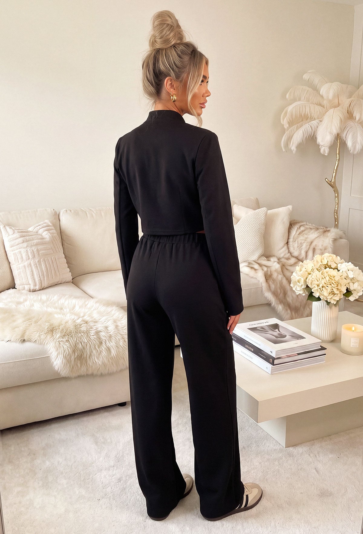Black wide leg trousers with an elasticated waistband and relaxed fit, styled with white trainers and a chain strap bag.